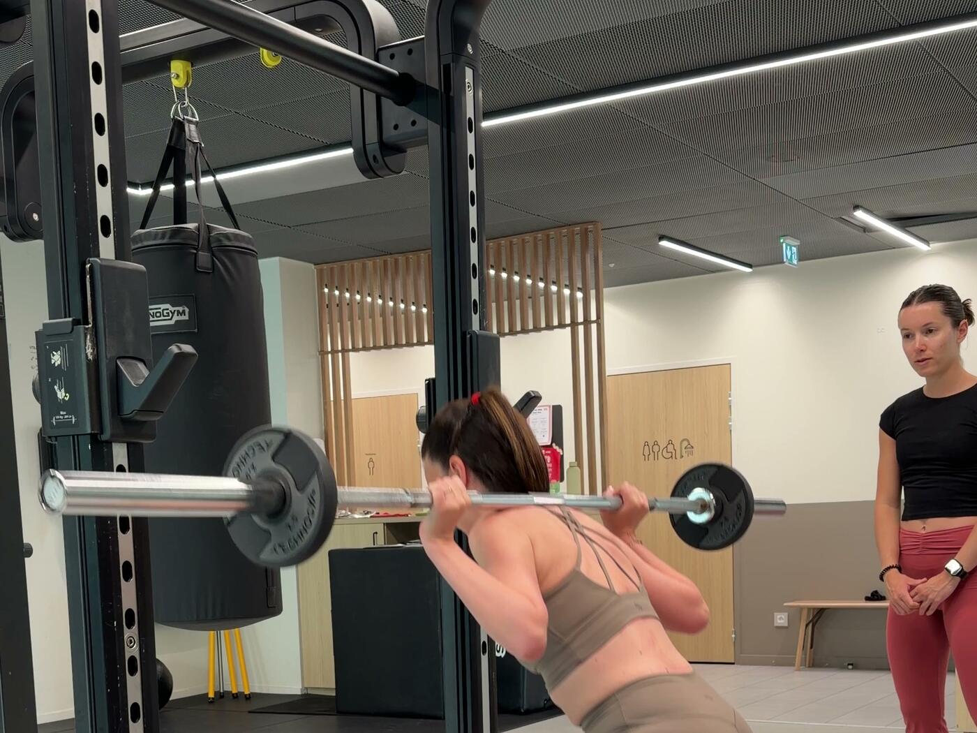 Jade Ribal corrige la posture d'une cliente pendant un squat à la barre